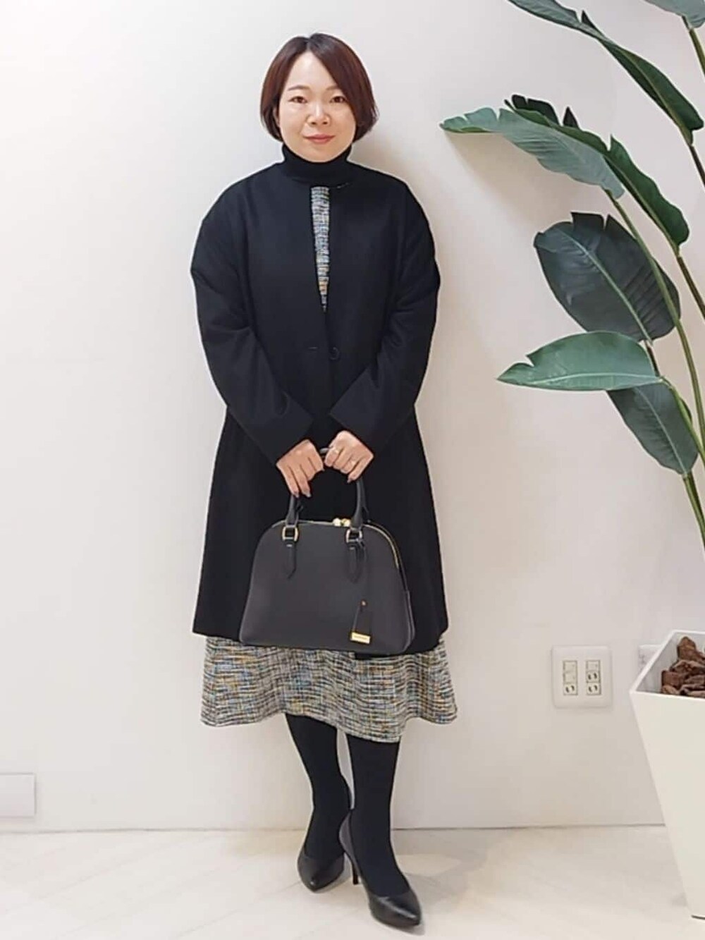 ブラック系のノーカラーコート、ブラック系のTシャツ/カットソー、ブラック系のスカートを着用したレディースの冬コーディネートの3枚目の写真