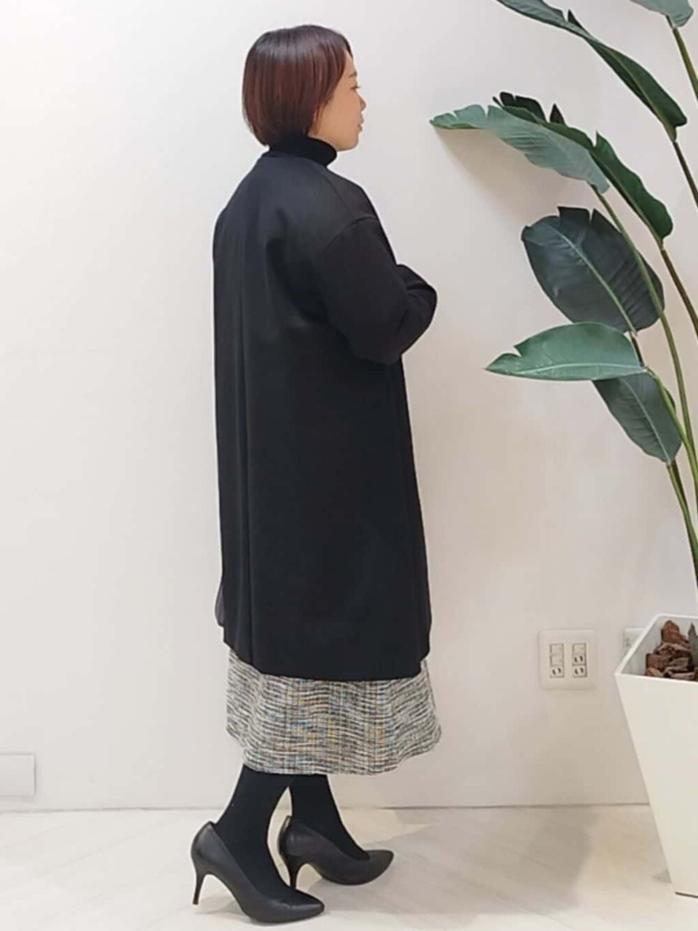ブラック系のノーカラーコート、ブラック系のTシャツ/カットソー、ブラック系のスカートを着用したレディースの冬コーディネートの5枚目の写真