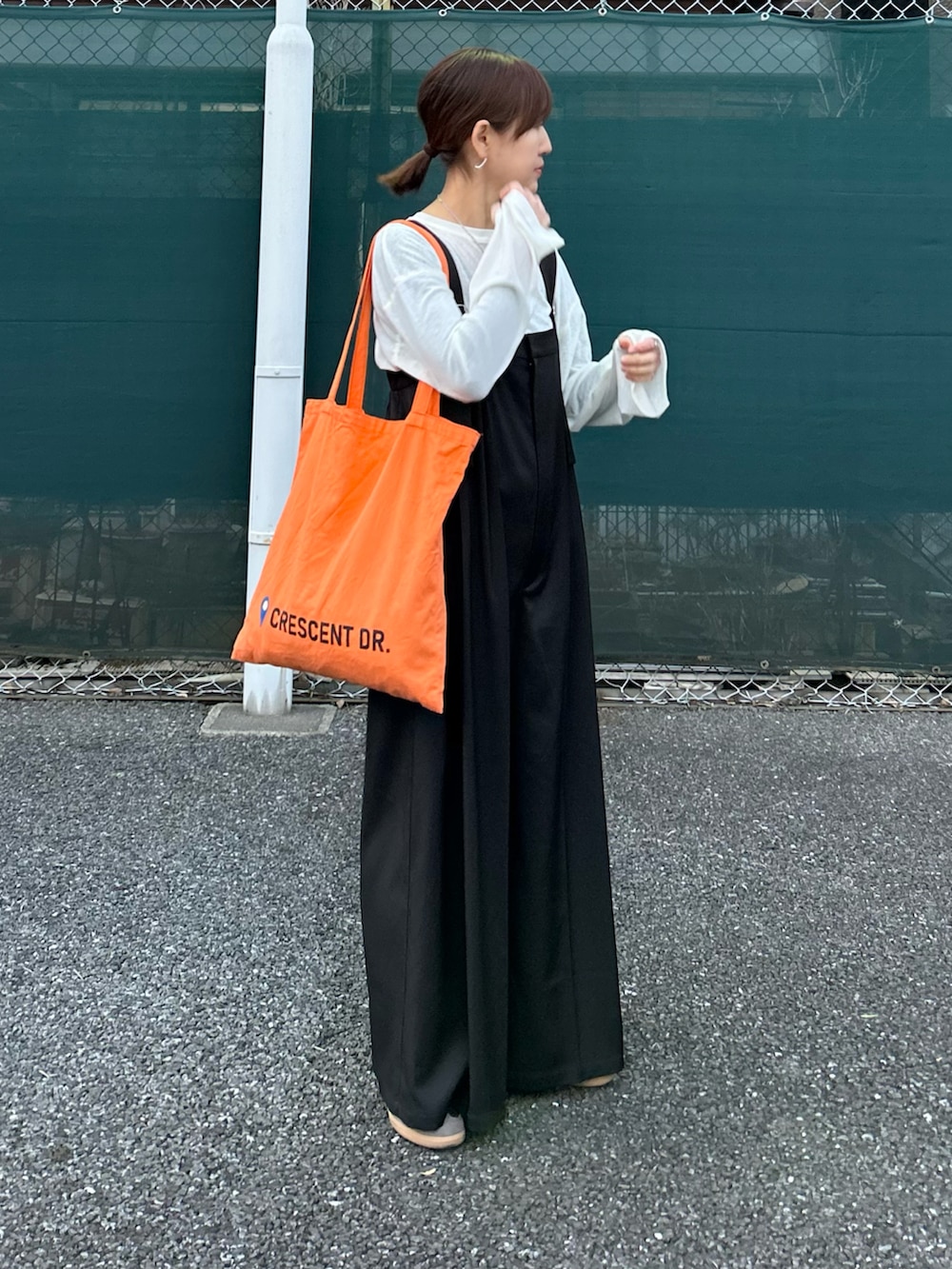 ブラック系のサロペット/オーバーオール、ホワイト系のTシャツ/カットソー、オレンジ系のトートバッグを着用したレディースの春コーディネートの3枚目の写真