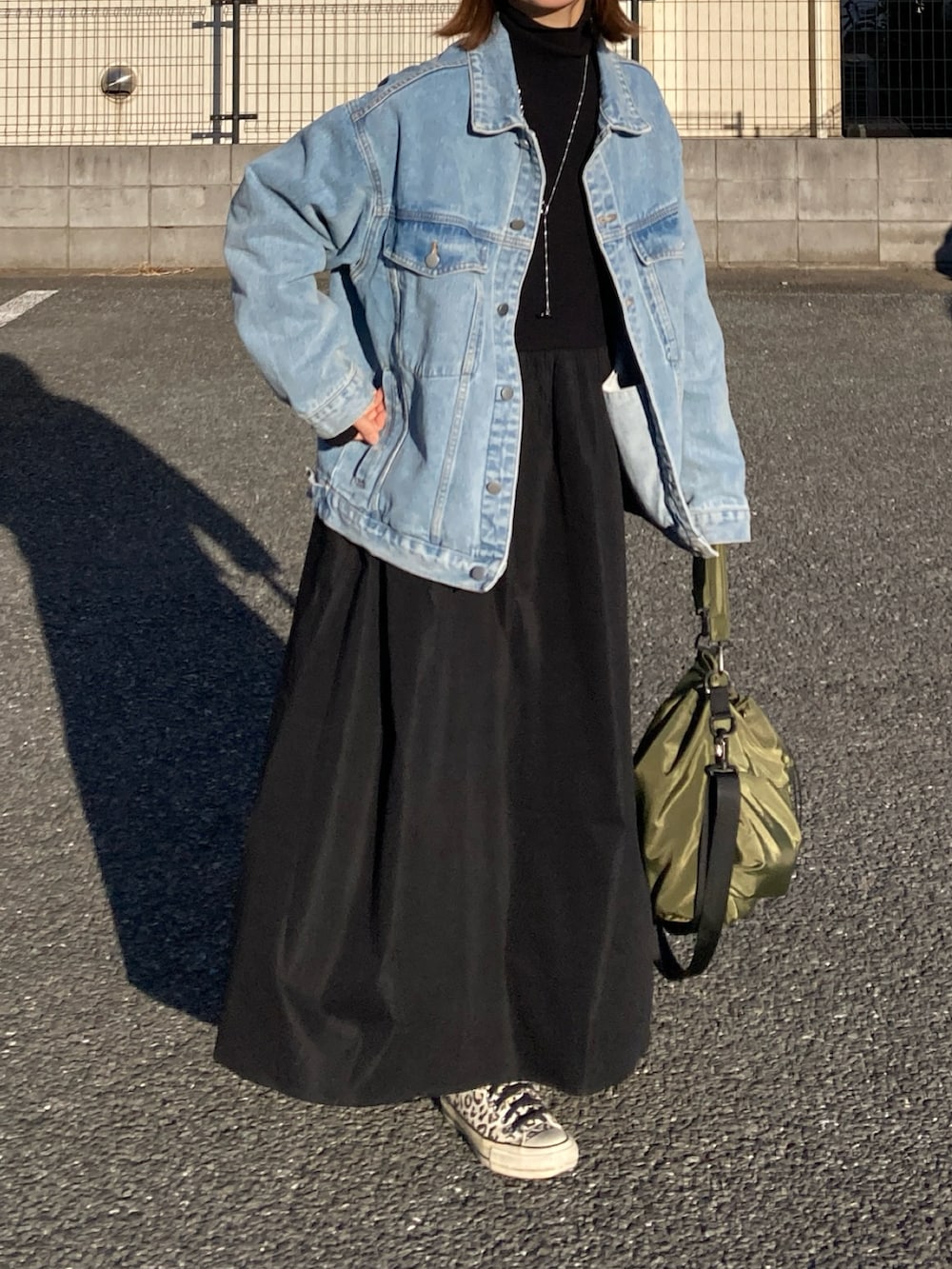 ブルー系のデニムジャケット、ブラック系のワンピース、グリーン系のショルダーバッグを着用したレディースの冬コーディネートの2枚目の写真