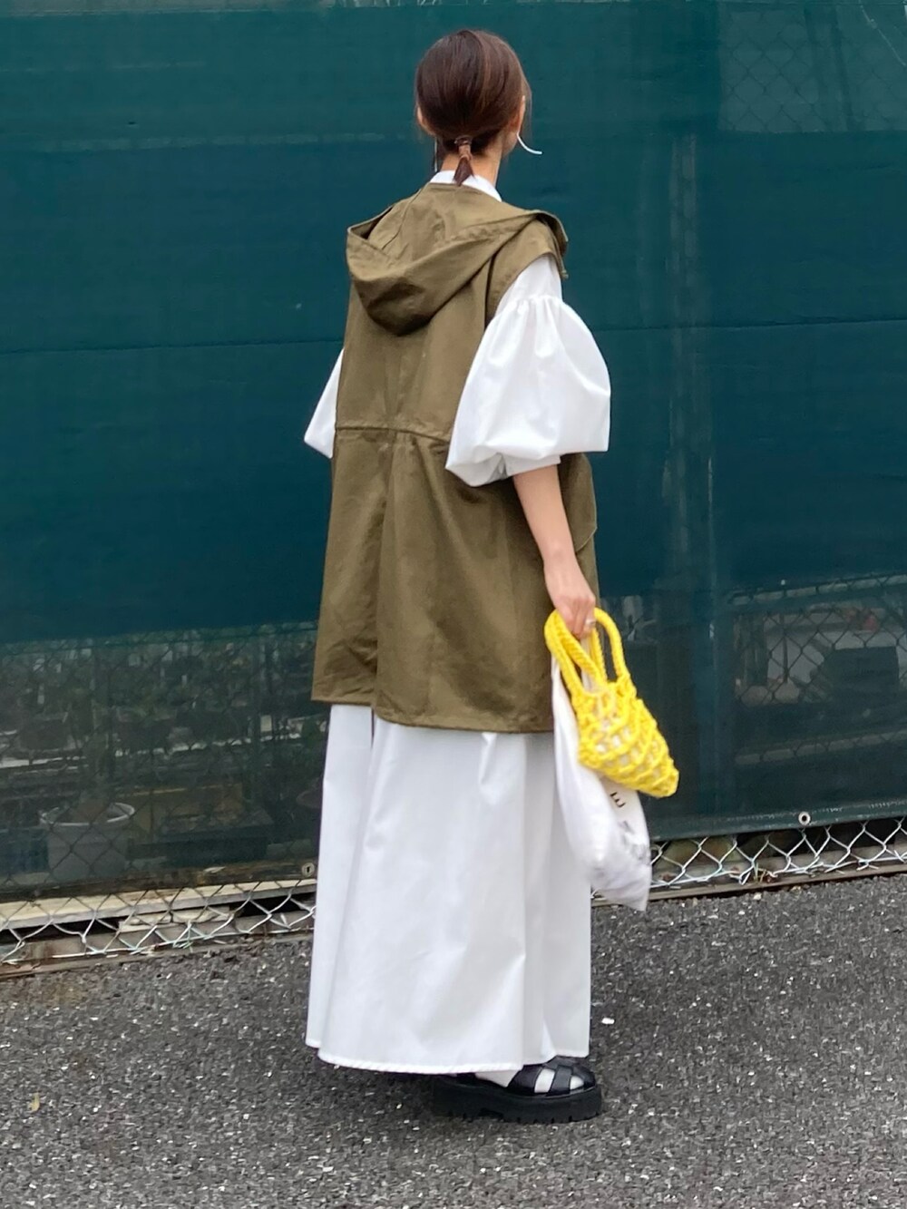 グリーン系のミリタリージャケット、ホワイト系のワンピース、イエロー系のハンドバッグを着用したレディースの春コーディネートの5枚目の写真