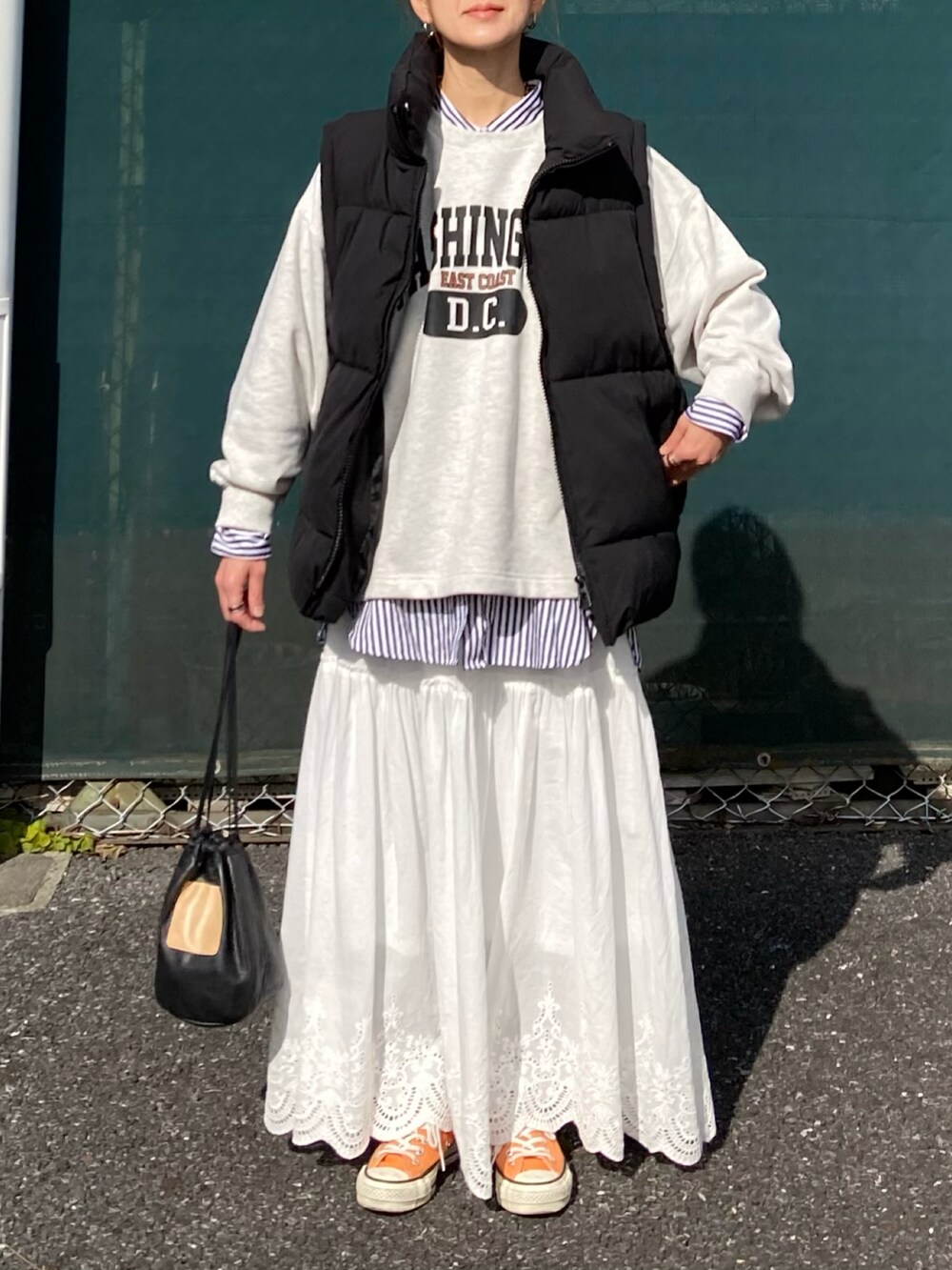 ブラック系のダウンベスト、ベージュ系のスウェット、ホワイト系のスカートを着用したレディースの冬コーディネートの2枚目の写真