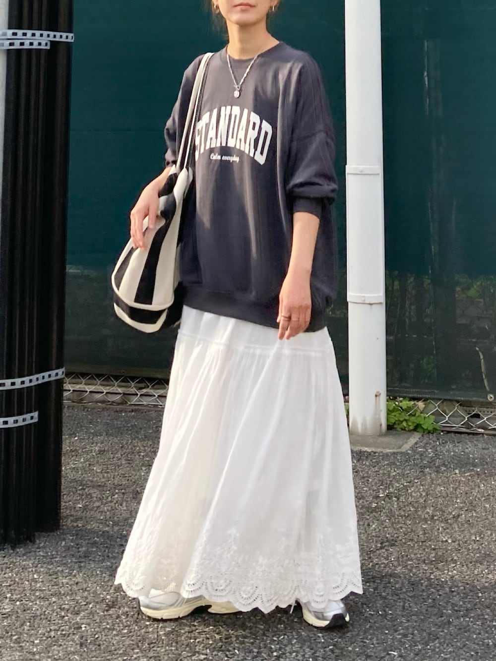 ブラック系のスウェット、ブラック系のトートバッグ、ホワイト系のスカートを着用したレディースの春コーディネートの3枚目の写真