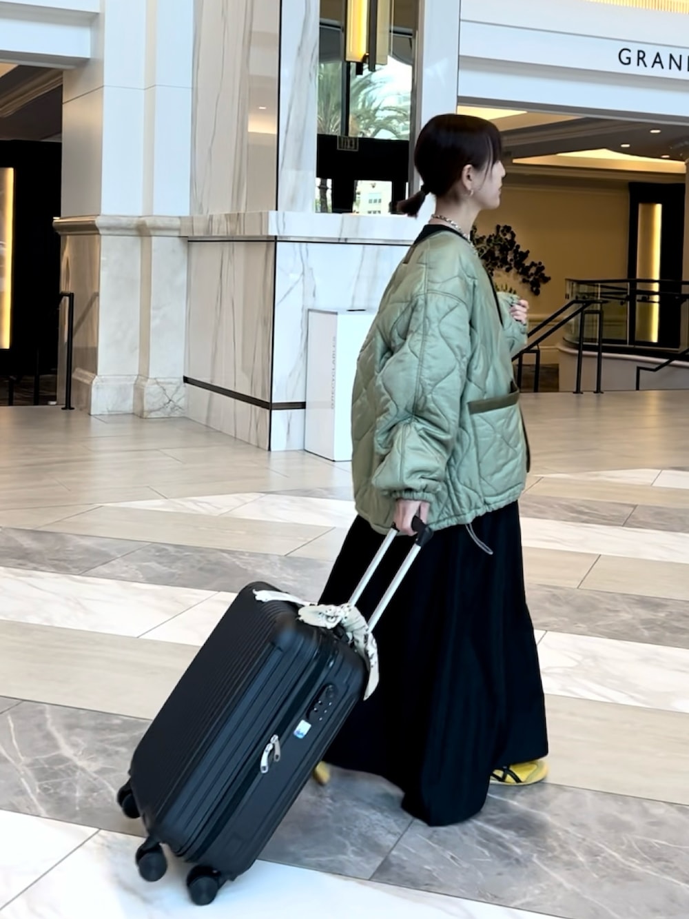 グリーン系のノーカラージャケット、ブラック系のワンピース、ブラック系のスーツケース/キャリーバッグを着用したレディースの春コーディネートの2枚目の写真