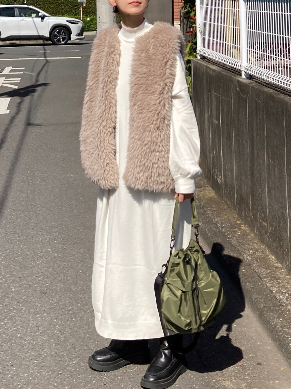 ホワイト系のワンピース、ベージュ系のベスト、グリーン系のショルダーバッグを着用したレディースの秋コーディネートの3枚目の写真