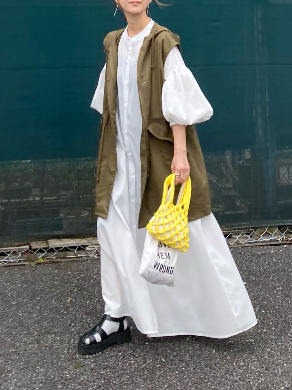 グリーン系のミリタリージャケット、ホワイト系のワンピース、イエロー系のハンドバッグを着用したレディースの春コーディネートの2枚目の写真