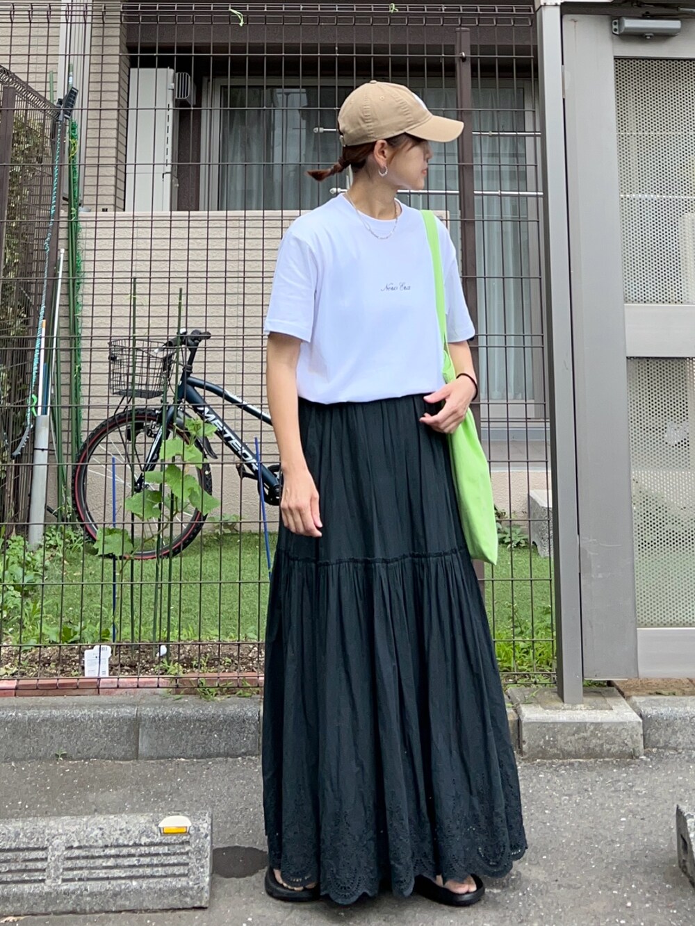 ブラック系のスカート、グリーン系のトートバッグ、ホワイト系のTシャツ/カットソーを着用したレディースの夏コーディネートの2枚目の写真