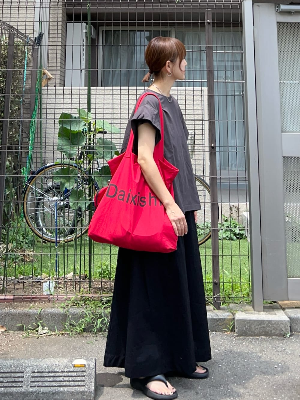 レッド系のトートバッグ、ブラック系のスカート、グレー系のTシャツ/カットソーを着用したレディースの夏コーディネートの2枚目の写真