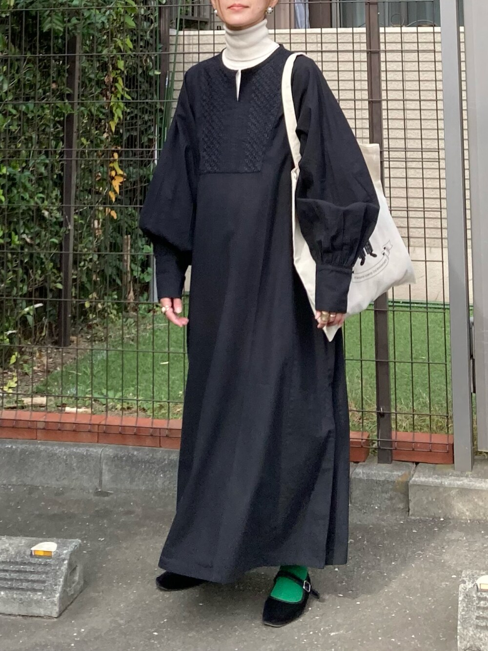 ブラック系のワンピース、ホワイト系のトートバッグ、ゴールド系のピアス（両耳用）を着用したレディースの秋コーディネートの2枚目の写真