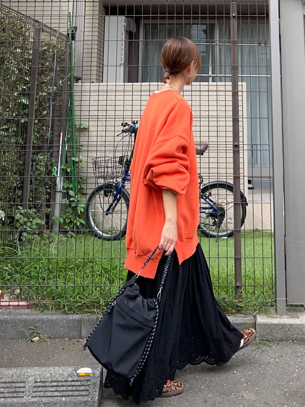 オレンジ系のスウェット、ブラック系のトートバッグ、ブラック系のスカートを着用したレディースの春コーディネートの2枚目の写真