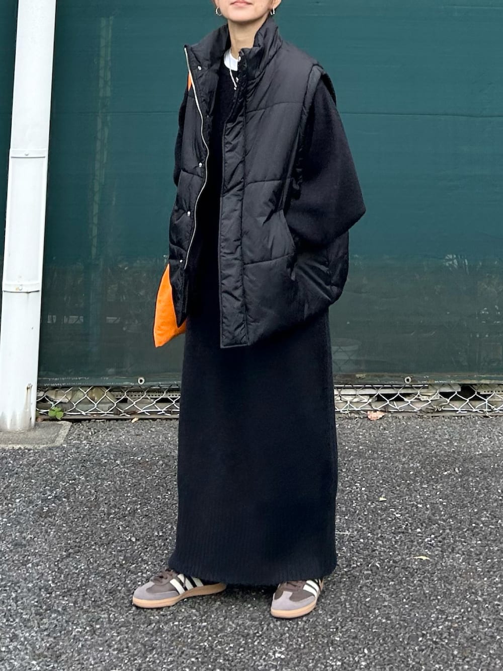 ブラック系のワンピース、ブラック系のダウンベスト、オレンジ系のトートバッグを着用したレディースの冬コーディネートの3枚目の写真