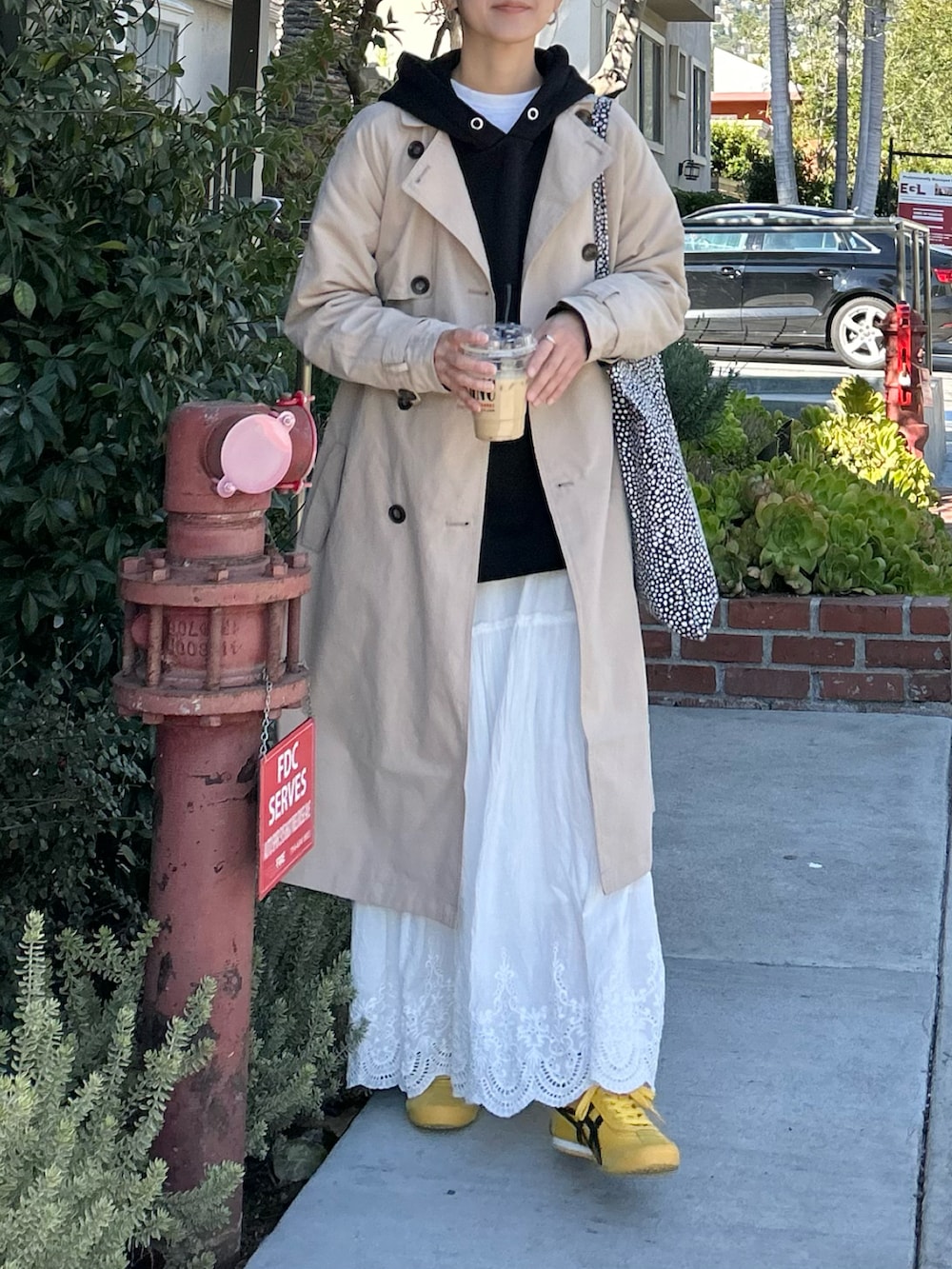 ベージュ系のトレンチコート、ブラック系のパーカー、ホワイト系のスカートを着用したレディースの冬コーディネートの3枚目の写真