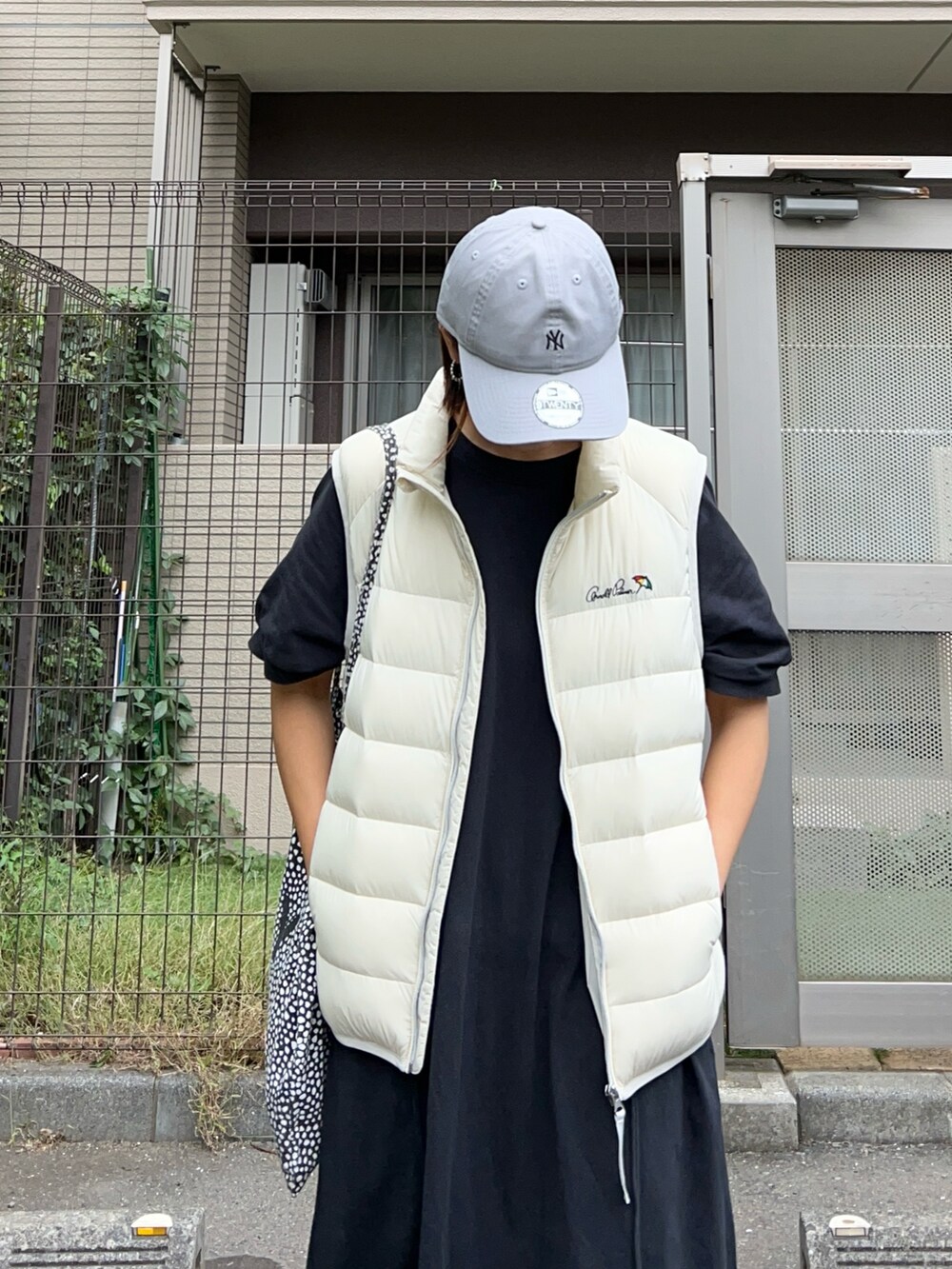 ホワイト系のダウンベスト、ブラック系のワンピース、ホワイト系のスニーカーを着用したレディースの秋コーディネートの4枚目の写真