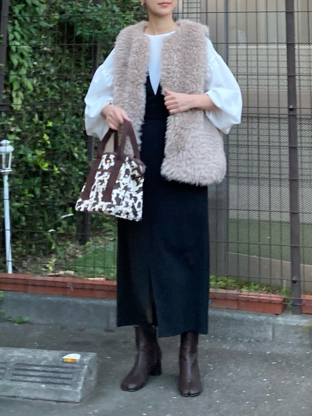 ベージュ系のベスト、ホワイト系のシャツ/ブラウス、ブラック系のジャンパースカートを着用したレディースの秋コーディネートの2枚目の写真