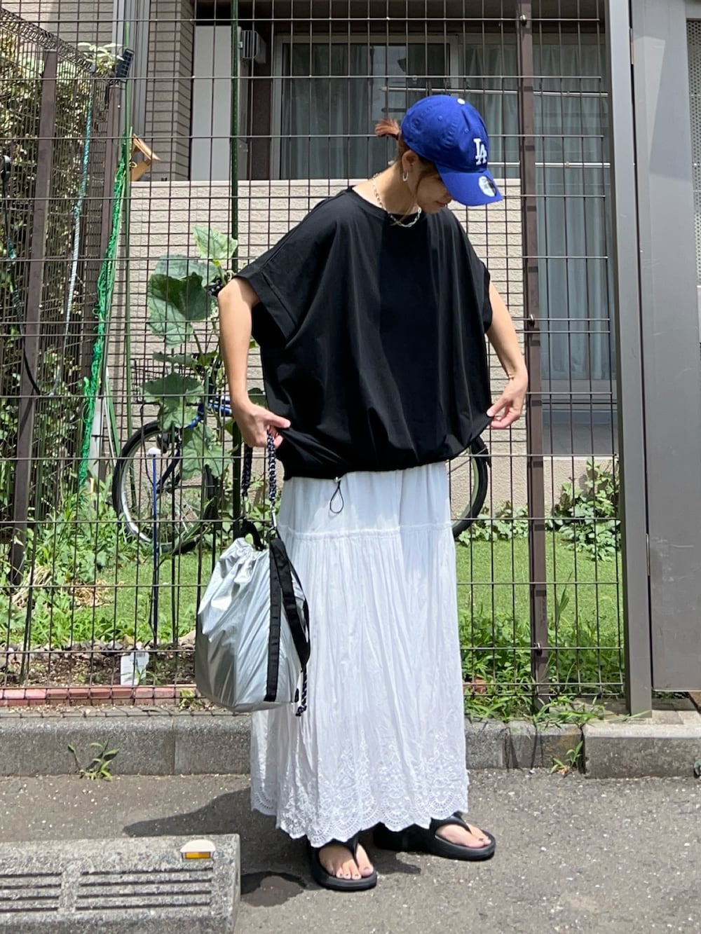 シルバー系のトートバッグ、ブラック系のTシャツ/カットソー、ホワイト系のスカートを着用したレディースの夏コーディネートの3枚目の写真