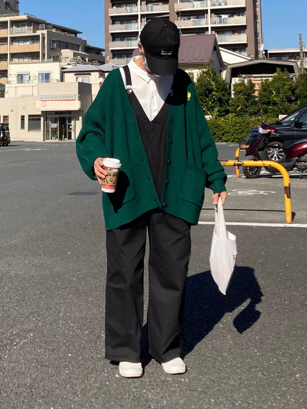 グリーン系のカーディガン/ボレロ、ホワイト系のシャツ/ブラウス、ブラック系のサロペット/オーバーオールを着用したレディースの秋コーディネートの2枚目の写真
