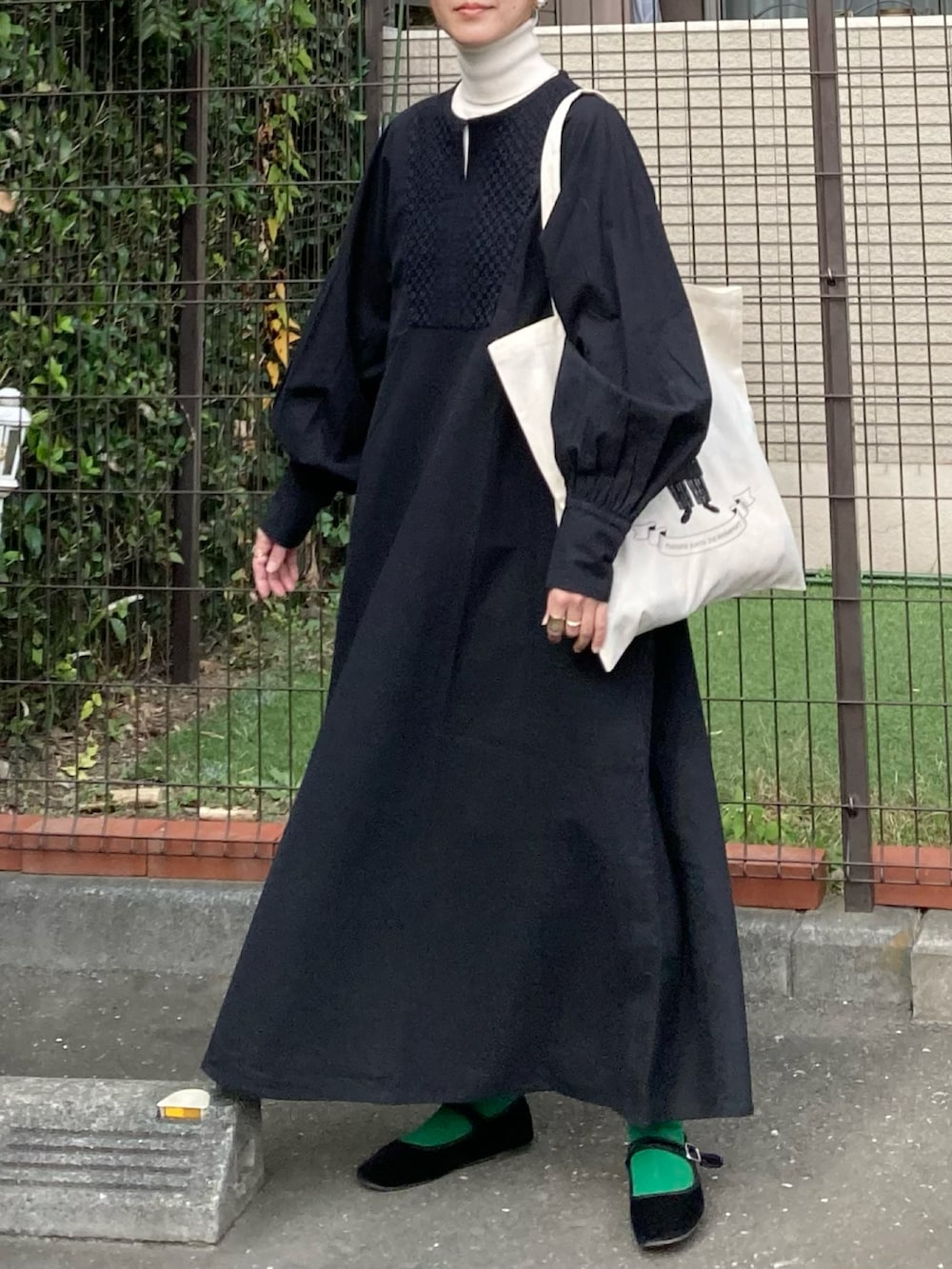 ブラック系のワンピース、ホワイト系のトートバッグ、ゴールド系のピアス（両耳用）を着用したレディースの秋コーディネートの3枚目の写真