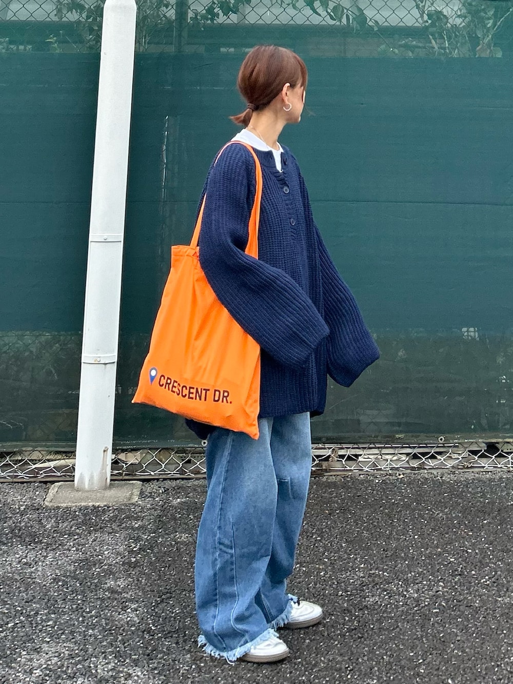 ブルー系のニット/セーター、オレンジ系のトートバッグ、ブルー系のデニムパンツを着用したレディースの秋コーディネートの2枚目の写真