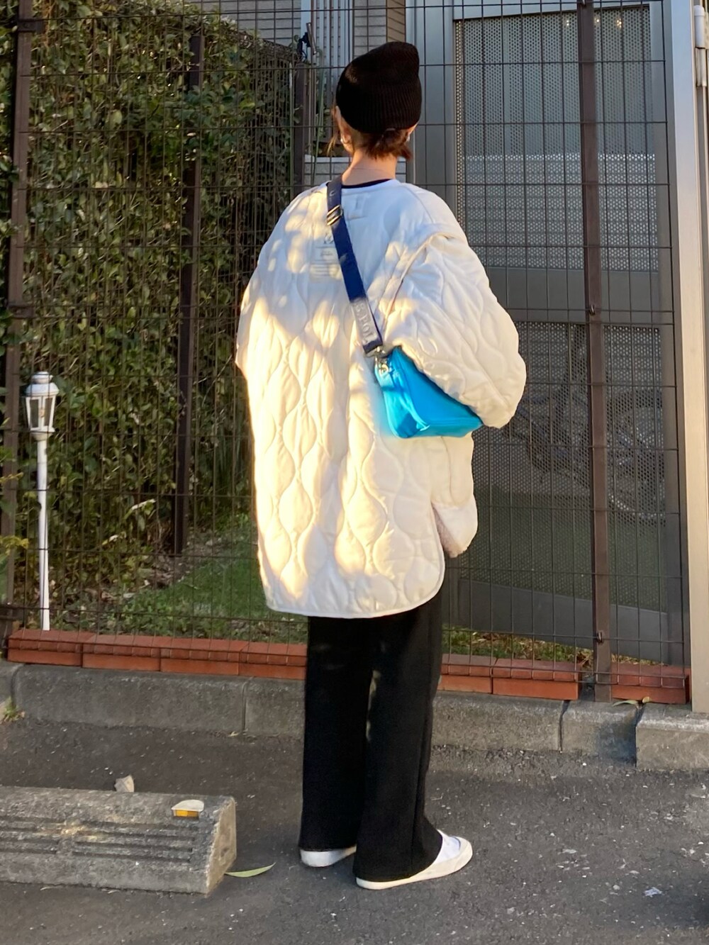 ホワイト系のブルゾン、ブルー系のショルダーバッグ、ブラック系のTシャツ/カットソーを着用したレディースの冬コーディネートの2枚目の写真