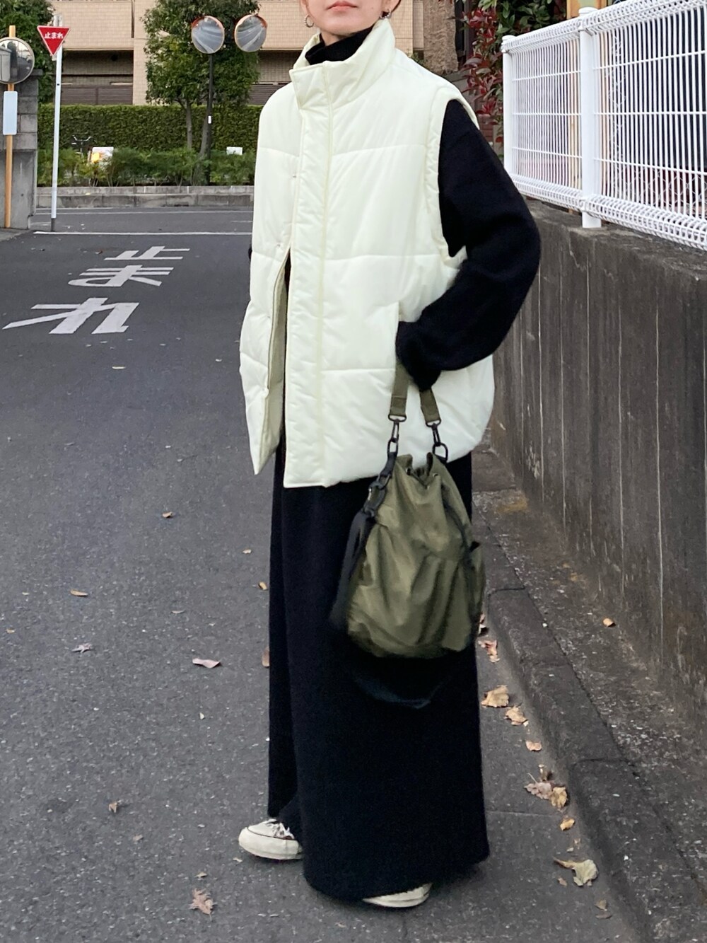 ホワイト系のダウンベスト、ブラック系のワンピース、グリーン系のショルダーバッグを着用したレディースの冬コーディネートの4枚目の写真