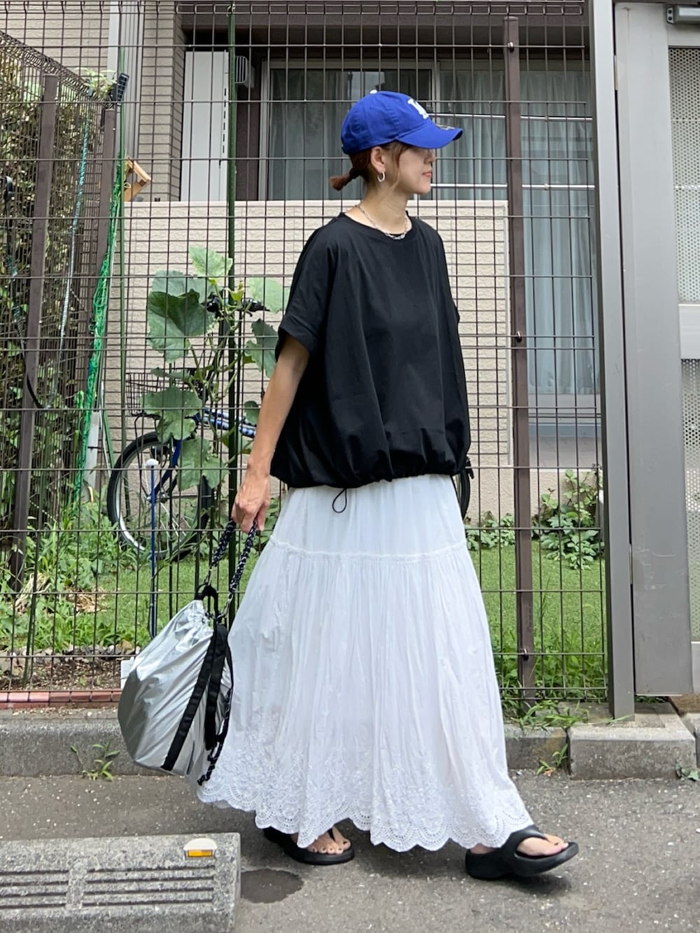 シルバー系のトートバッグ、ブラック系のTシャツ/カットソー、ホワイト系のスカートを着用したレディースの夏コーディネートの4枚目の写真