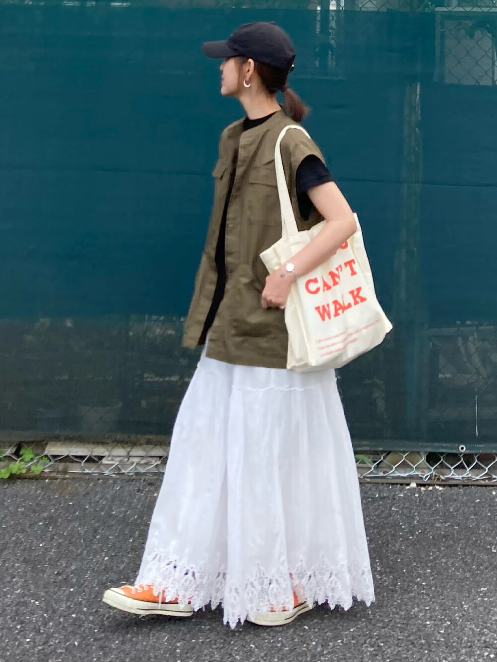 グリーン系のベスト、ブラック系のTシャツ/カットソー、ベージュ系のトートバッグを着用したレディースの夏コーディネートの2枚目の写真