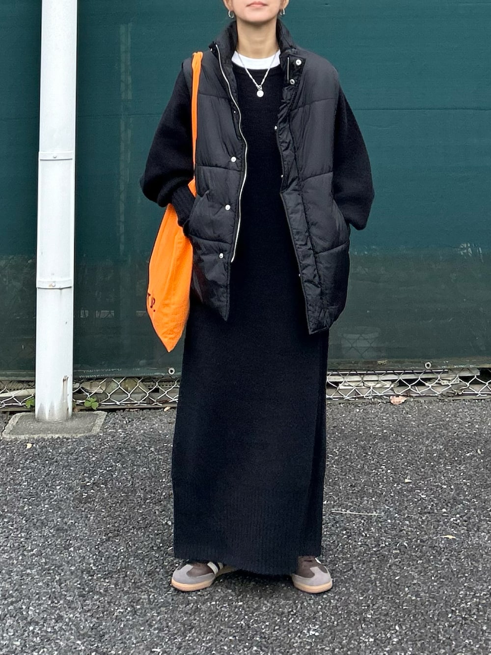 ブラック系のワンピース、ブラック系のダウンベスト、オレンジ系のトートバッグを着用したレディースの冬コーディネートの2枚目の写真