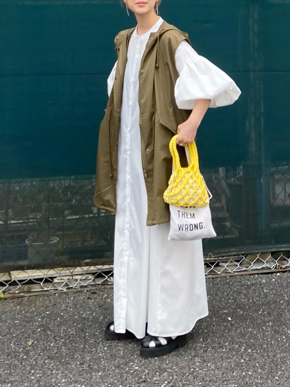 グリーン系のミリタリージャケット、ホワイト系のワンピース、イエロー系のハンドバッグを着用したレディースの春コーディネートの3枚目の写真