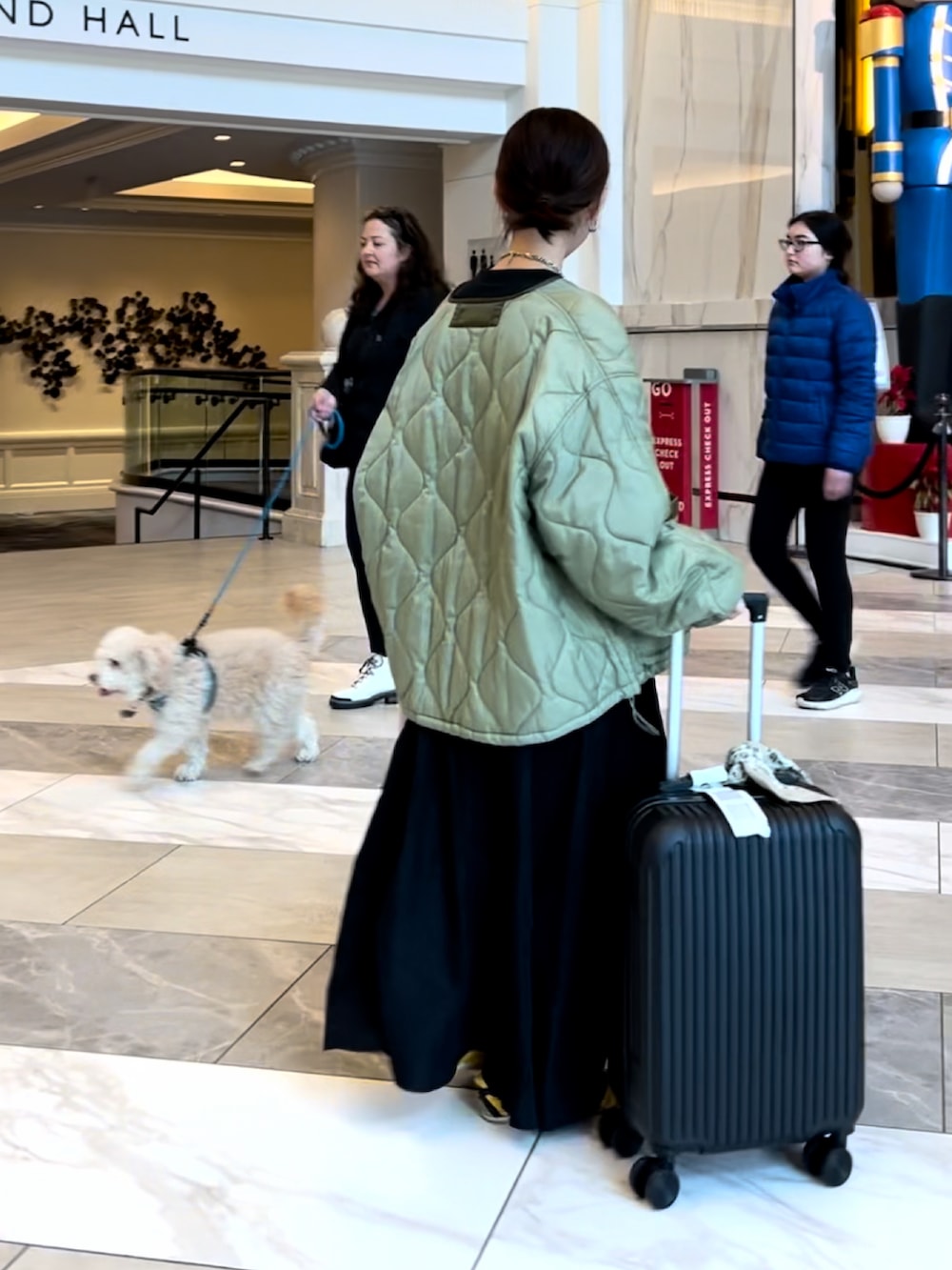 グリーン系のノーカラージャケット、ブラック系のワンピース、ブラック系のスーツケース/キャリーバッグを着用したレディースの春コーディネートの3枚目の写真