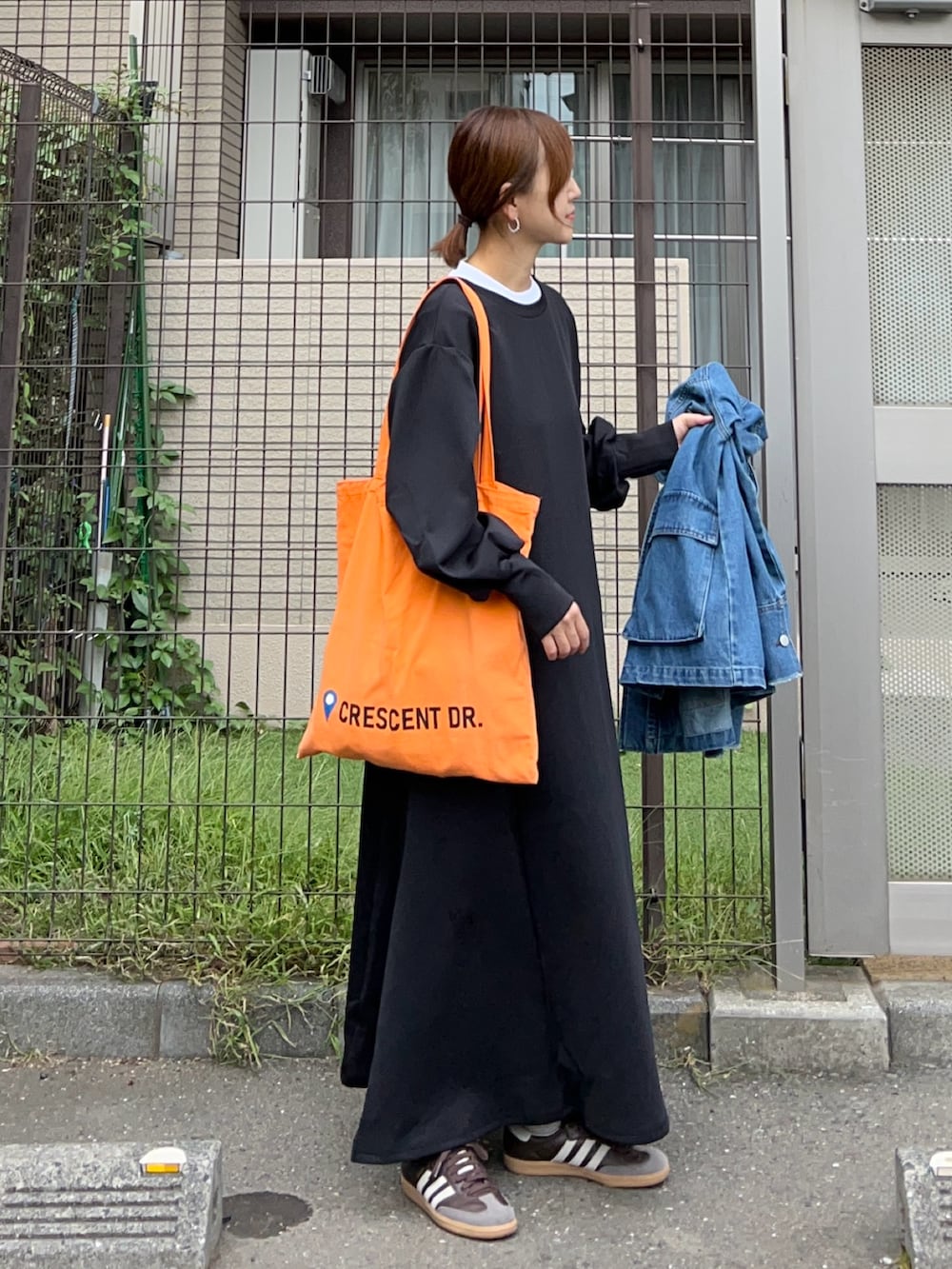 ブラック系のワンピース、オレンジ系のトートバッグ、ブラウン系のスニーカーを着用したレディースの秋コーディネートの2枚目の写真