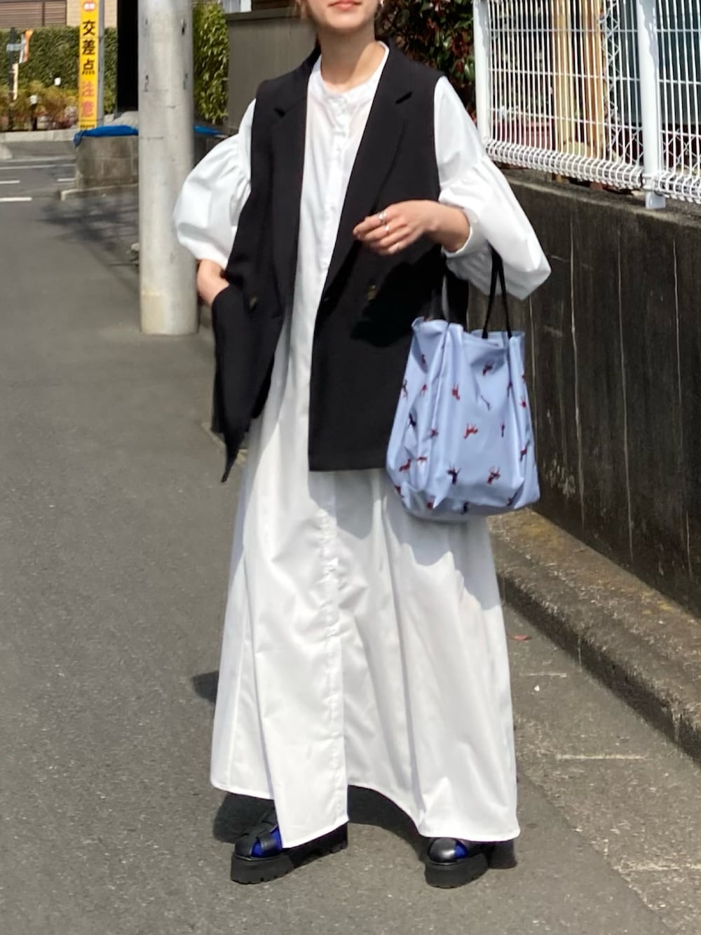 ホワイト系のワンピース、ブラック系のベスト、ブルー系のトートバッグを着用したレディースの春コーディネートの3枚目の写真