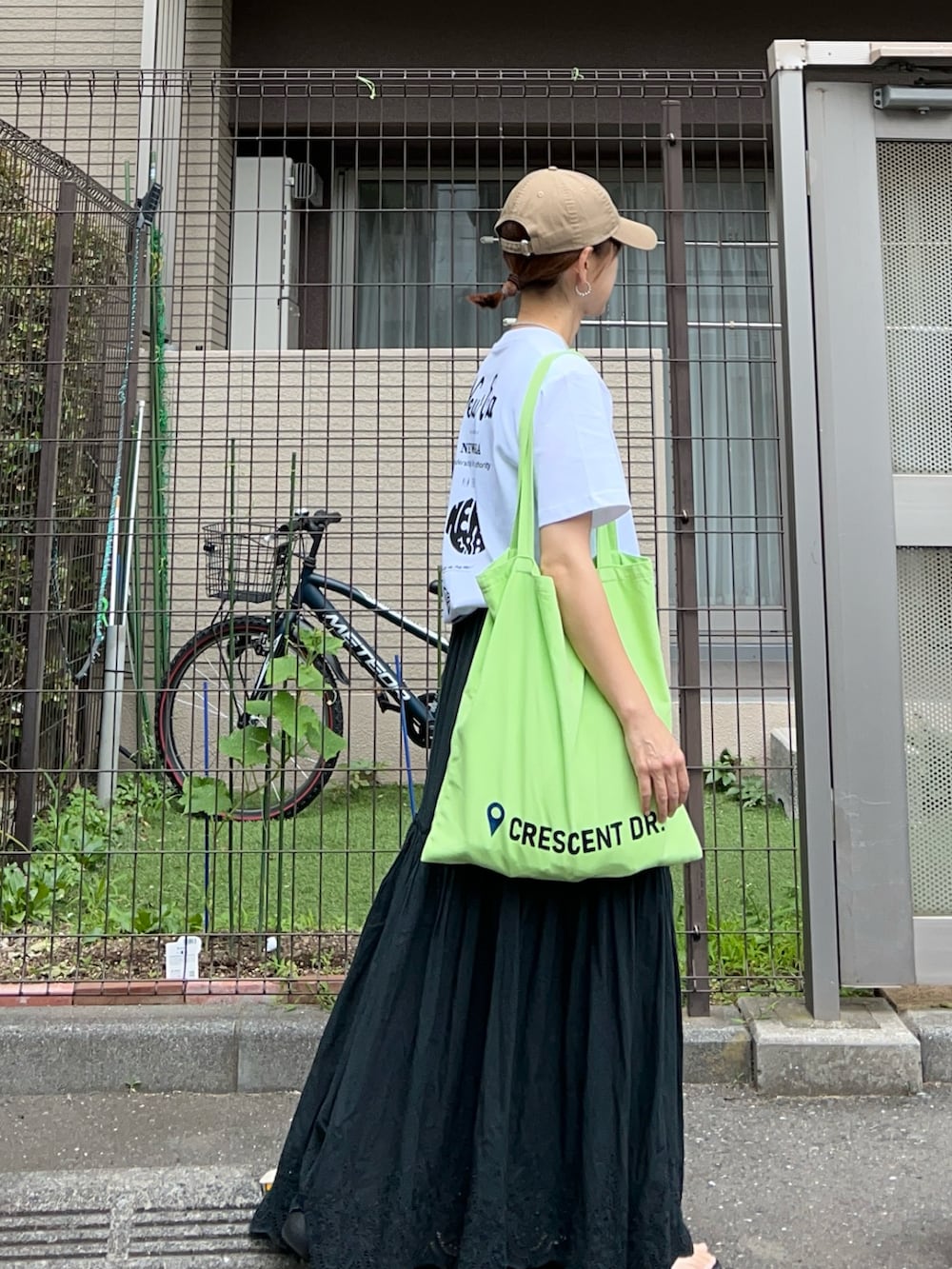 ブラック系のスカート、グリーン系のトートバッグ、ホワイト系のTシャツ/カットソーを着用したレディースの夏コーディネートの4枚目の写真