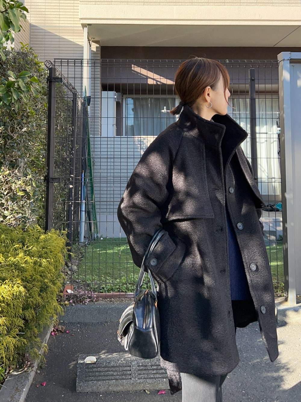 ブラック系のステンカラーコート、ブルー系のニット/セーター、ブラック系のその他パンツを着用したレディースの冬コーディネートの3枚目の写真