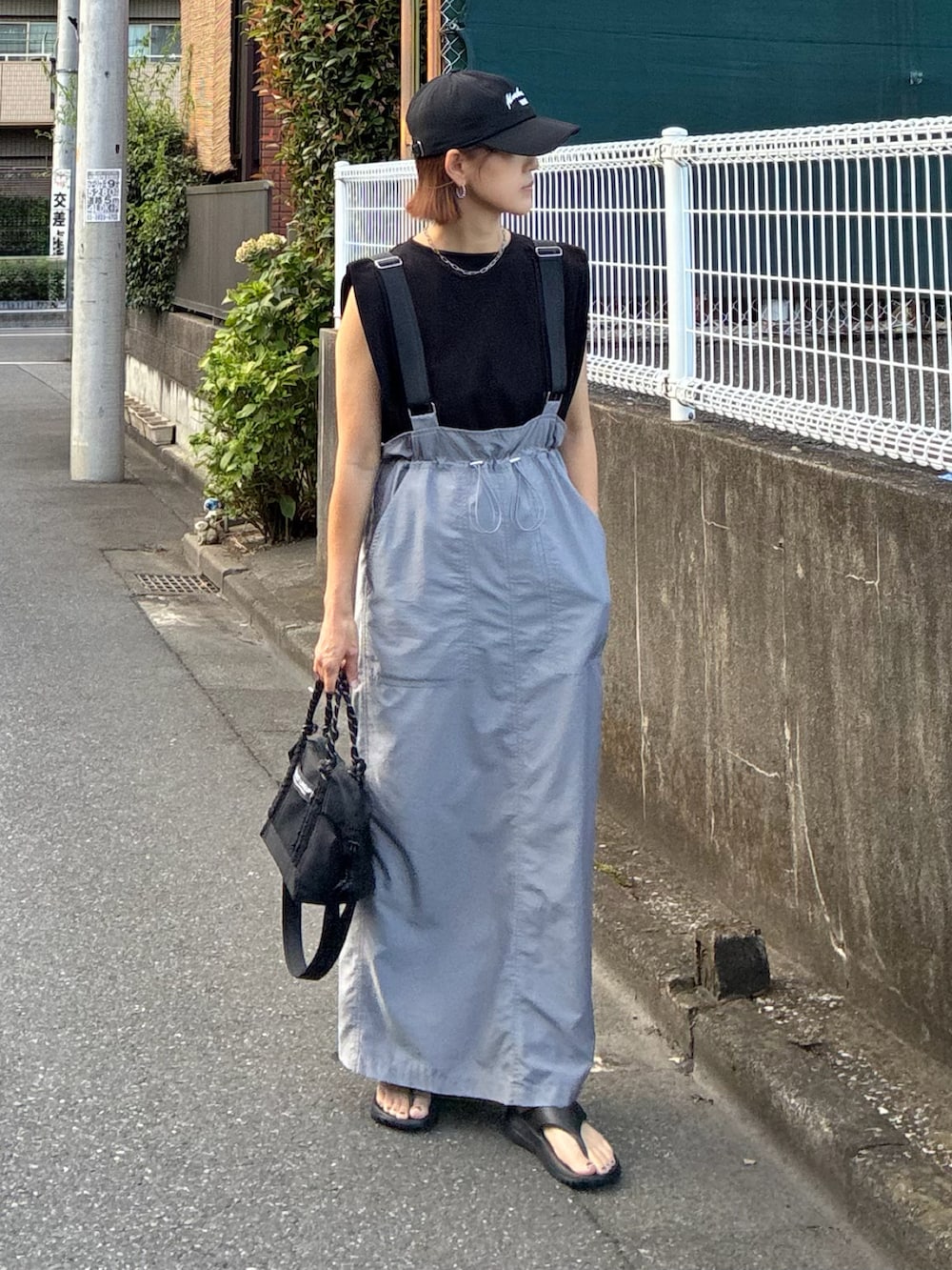 グレー系のジャンパースカート、ブラック系のサンダル、ブラック系のTシャツ/カットソーを着用したレディースの秋コーディネートの2枚目の写真