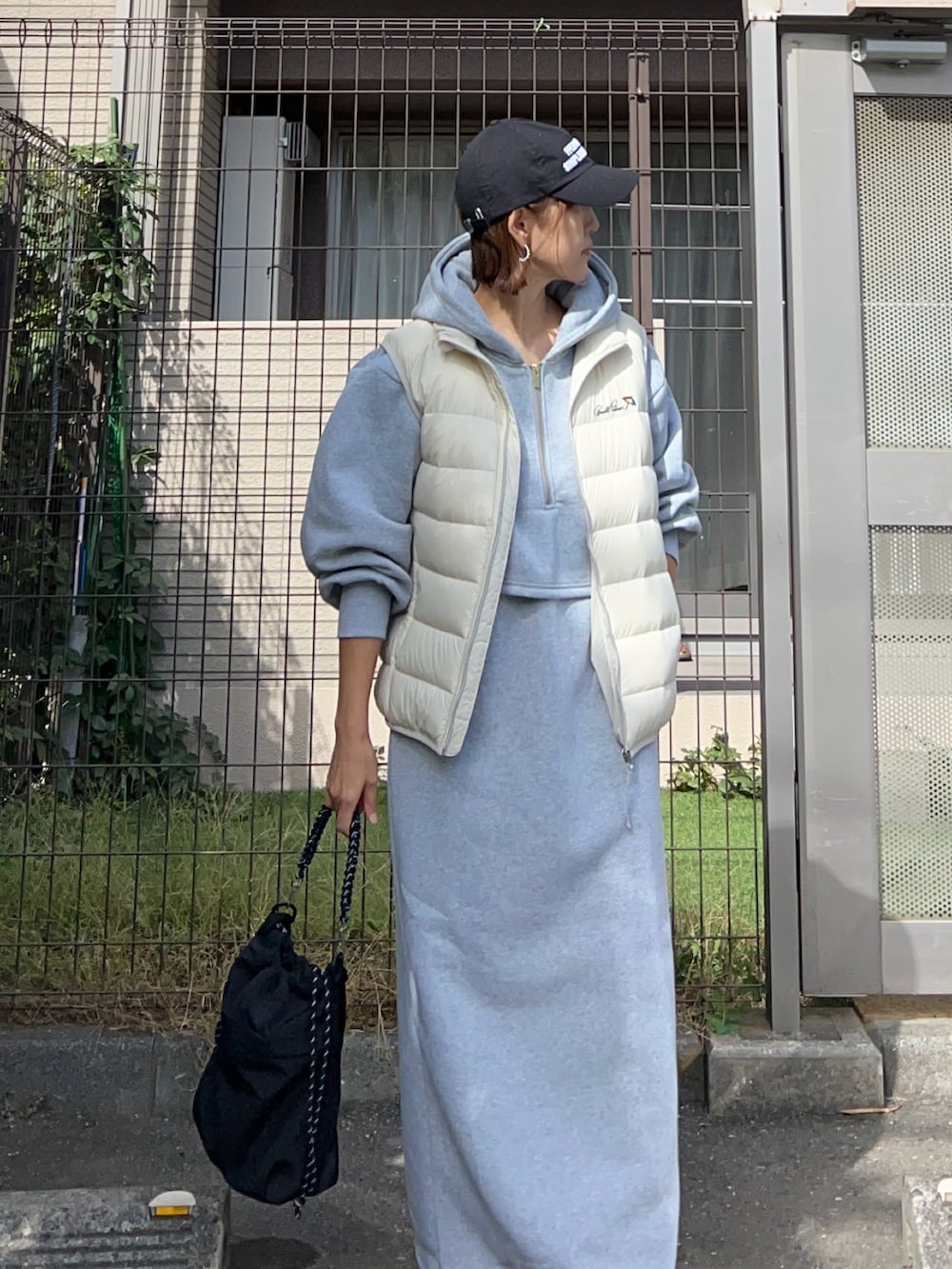 グレー系のワンピース、ブラック系のトートバッグ、ホワイト系のダウンベストを着用したレディースの秋コーディネートの3枚目の写真