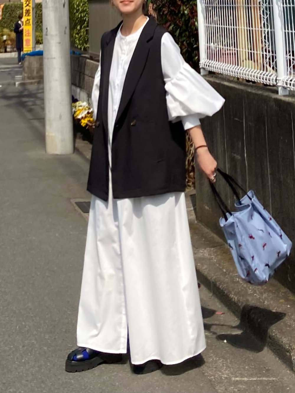 ホワイト系のワンピース、ブラック系のベスト、ブルー系のトートバッグを着用したレディースの春コーディネートの2枚目の写真