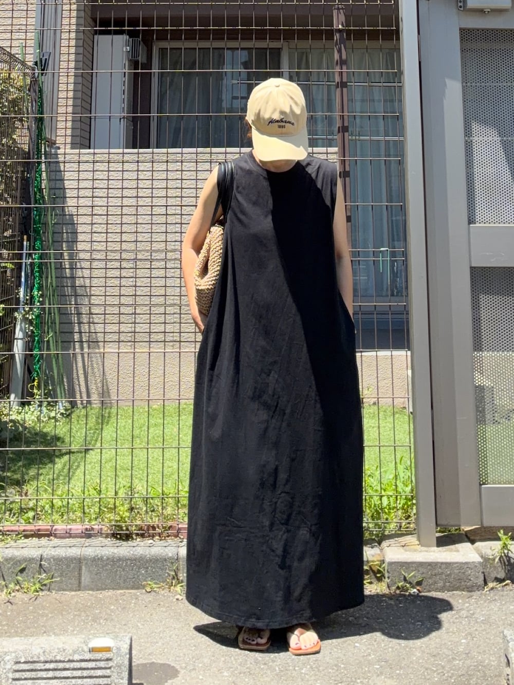 ブラック系のワンピース、イエロー系のトートバッグ、ベージュ系のキャップを着用したレディースの夏コーディネートの4枚目の写真