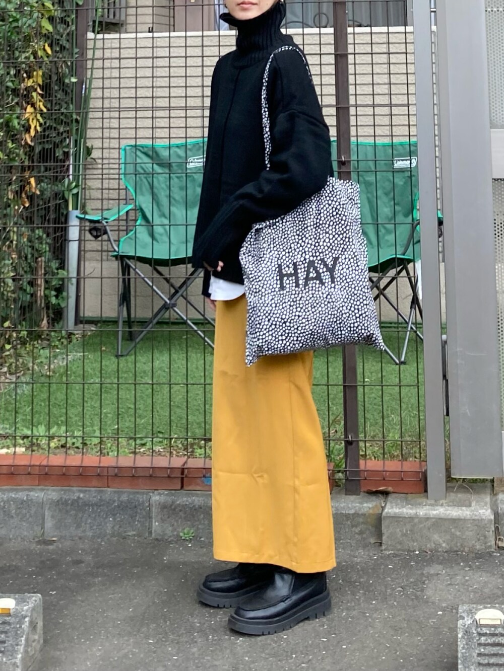 ブラック系のニット/セーター、イエロー系のスカート、ブラック系のブーツを着用したレディースの秋コーディネートの2枚目の写真