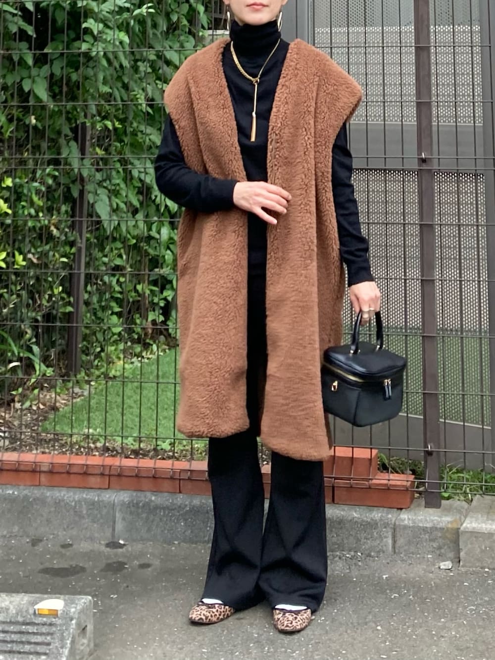 ブラウン系のベスト、ブラック系のショルダーバッグ、ゴールド系のネックレスを着用したレディースの秋コーディネートの2枚目の写真