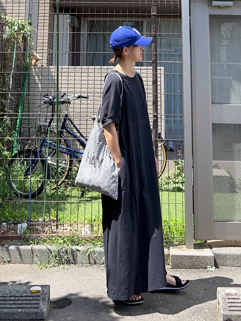 ブラック系のワンピース、ブラック系のサンダル、ブルー系のキャップを着用したレディースの夏コーディネートの2枚目の写真