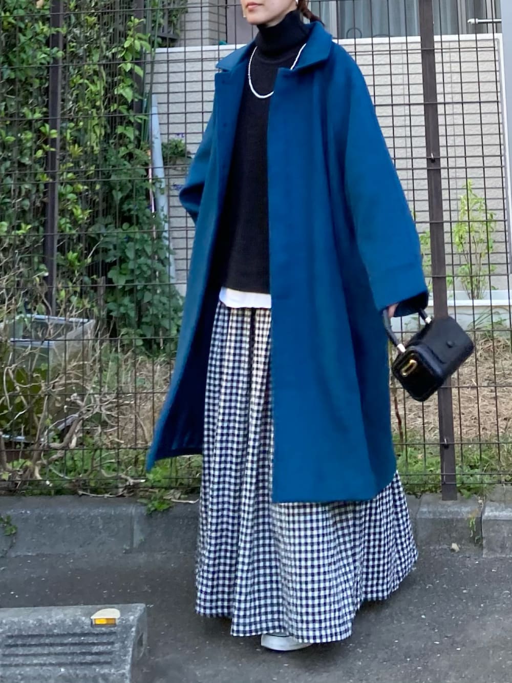 ブルー系のステンカラーコート、ブラック系のニット/セーター、ブラック系のスカートを着用したレディースの秋コーディネートの2枚目の写真