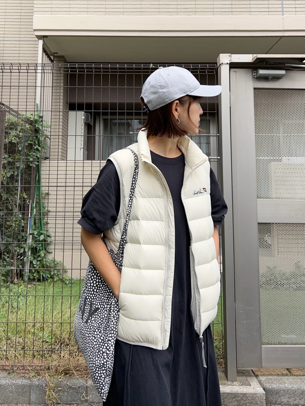 ホワイト系のダウンベスト、ブラック系のワンピース、ホワイト系のスニーカーを着用したレディースの秋コーディネートの3枚目の写真