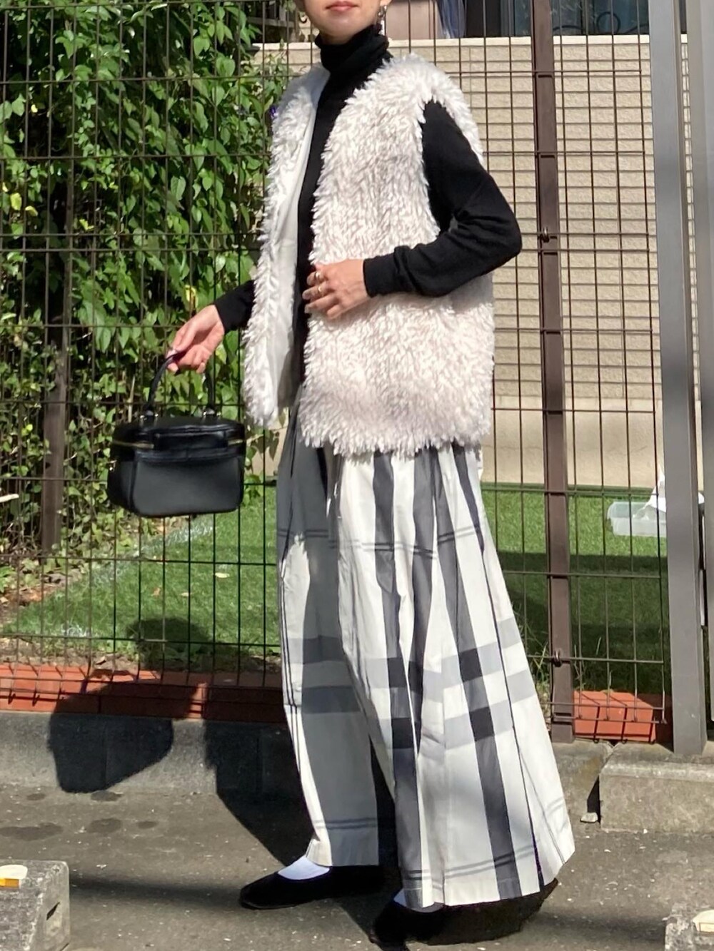 ホワイト系のベスト、ホワイト系のスカート、ブラック系のショルダーバッグを着用したレディースの秋コーディネートの3枚目の写真