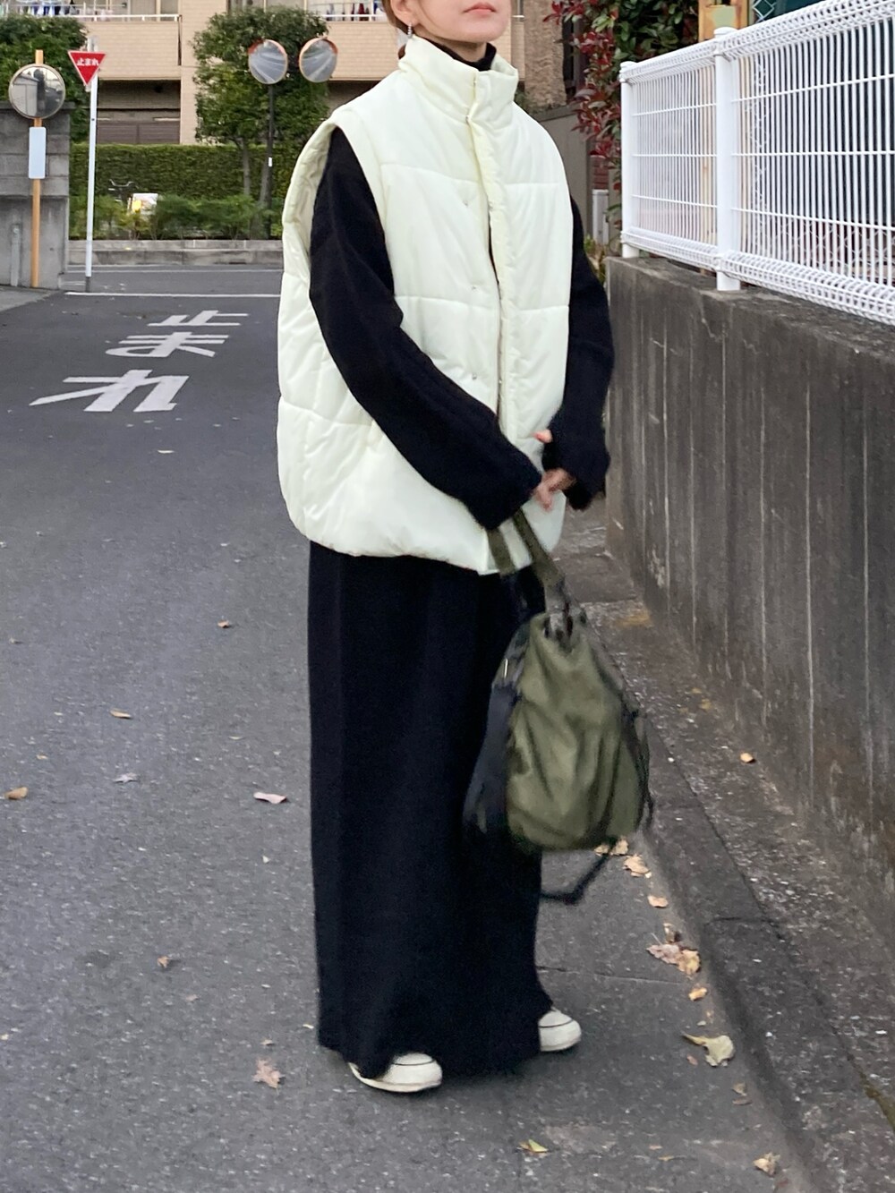 ホワイト系のダウンベスト、ブラック系のワンピース、グリーン系のショルダーバッグを着用したレディースの冬コーディネートの2枚目の写真