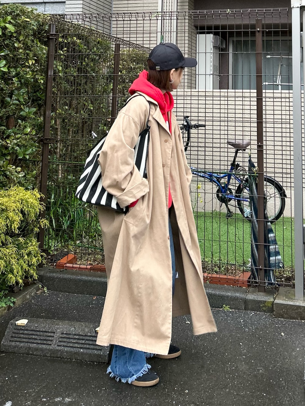 ブラック系のかごバッグ、ベージュ系のトレンチコート、ブルー系のデニムパンツを着用したレディースの春コーディネートの2枚目の写真