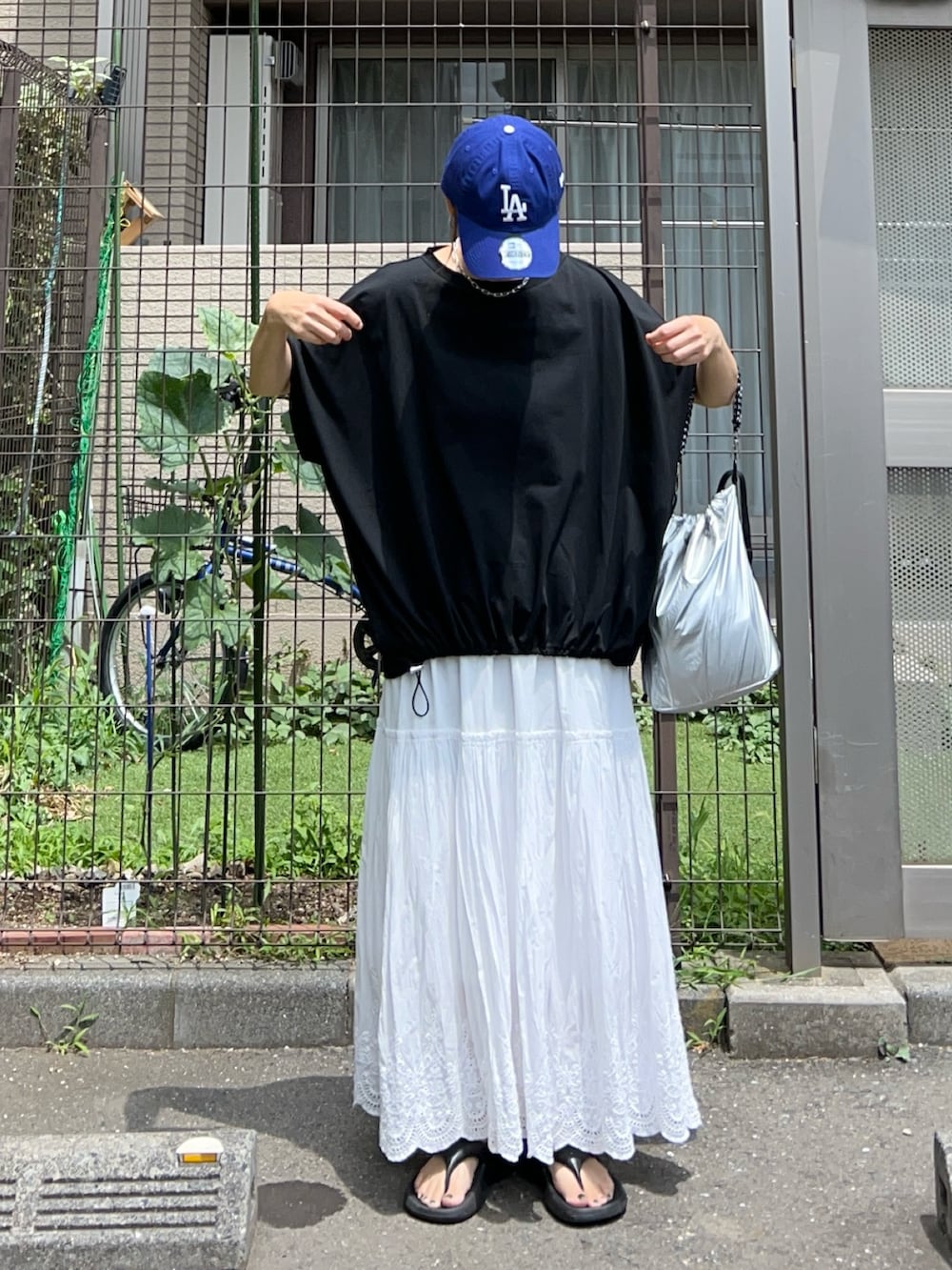 シルバー系のトートバッグ、ブラック系のTシャツ/カットソー、ホワイト系のスカートを着用したレディースの夏コーディネートの2枚目の写真