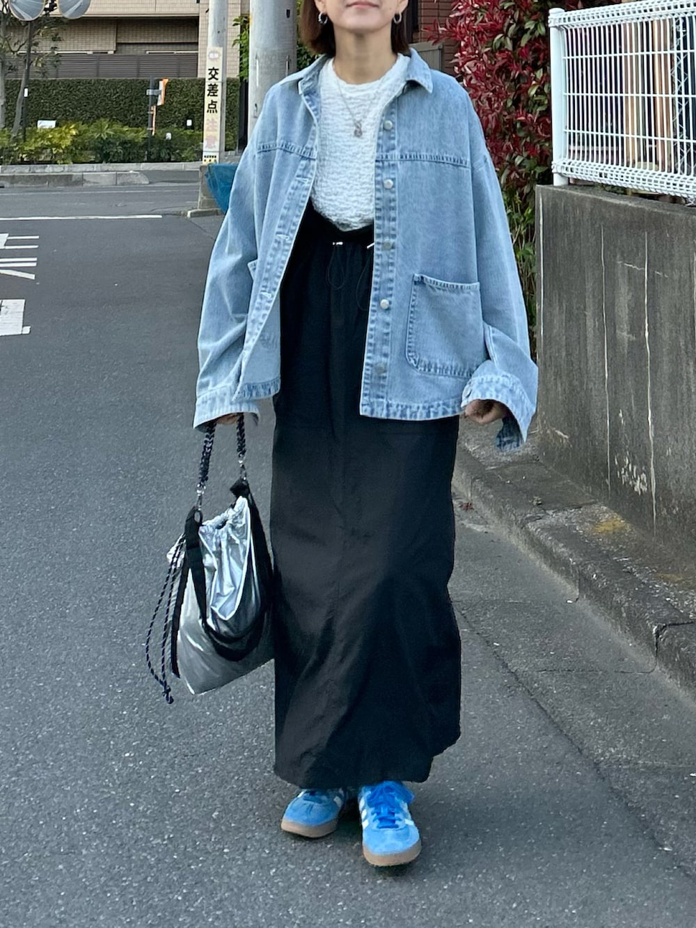 ブルー系のデニムジャケット、ブラック系のジャンパースカート、シルバー系のショルダーバッグを着用したレディースの春コーディネートの3枚目の写真