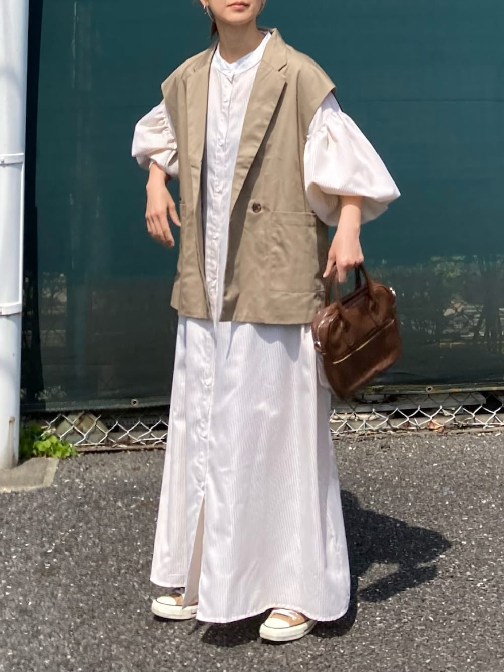 ベージュ系のベスト、ベージュ系のワンピース、ブラウン系のショルダーバッグを着用したレディースの春コーディネートの3枚目の写真