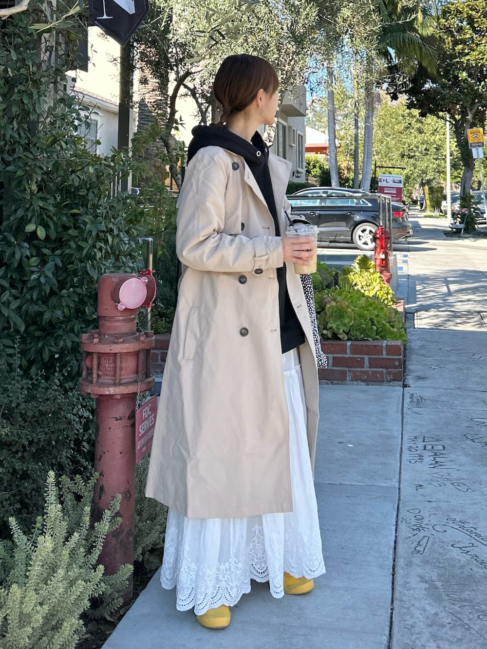 ベージュ系のトレンチコート、ブラック系のパーカー、ホワイト系のスカートを着用したレディースの冬コーディネートの2枚目の写真