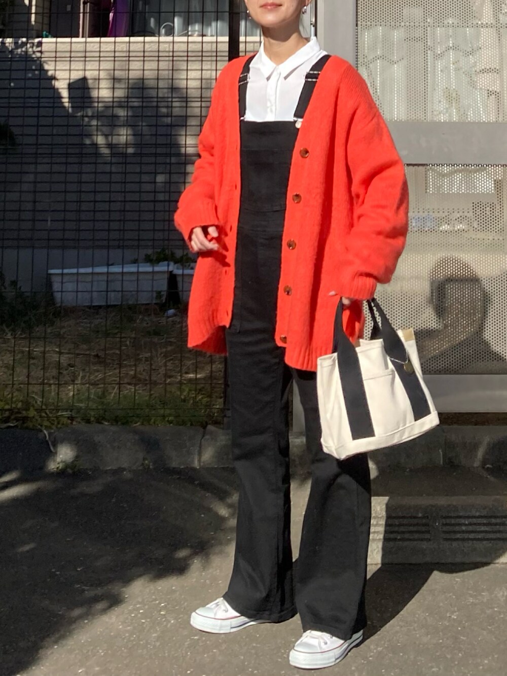 オレンジ系のカーディガン/ボレロ、ホワイト系のシャツ/ブラウス、ブラック系のサロペット/オーバーオールを着用したレディースの冬コーディネートの2枚目の写真